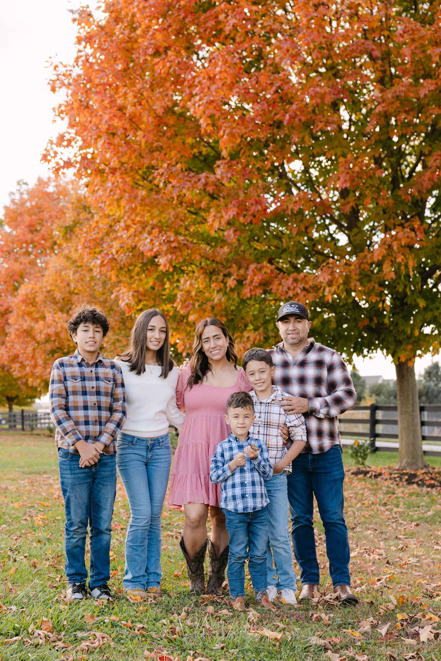 A family poses together outdoors against a rustic stone wall with autumn leaves scattered on the ground.