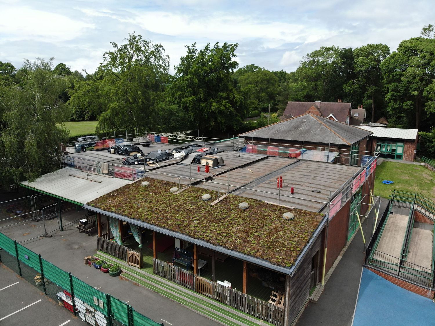 Aerial view of a flat-roofed building with a green sedum roof, surrounded by trees and a playground area.