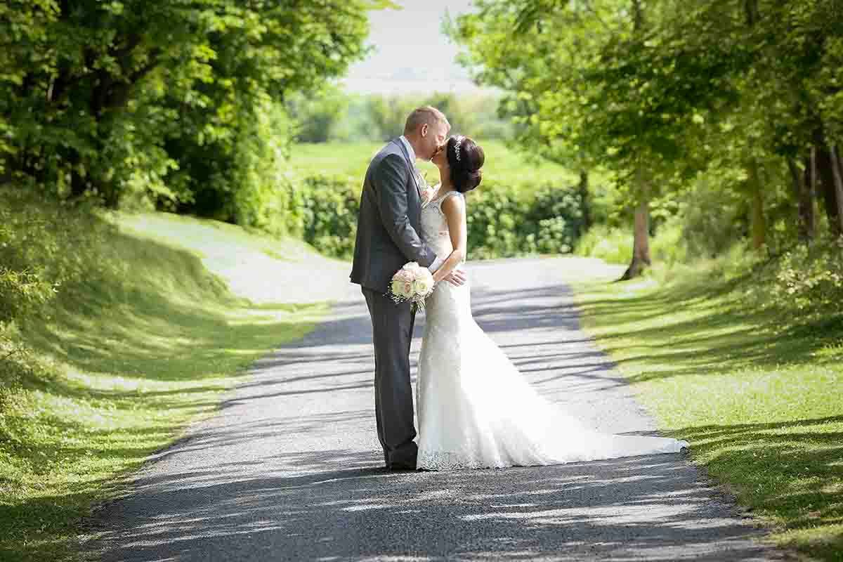 Bride and groom sharing a romantic kiss on a tree-lined path at Greenhill Hotel near Wigton