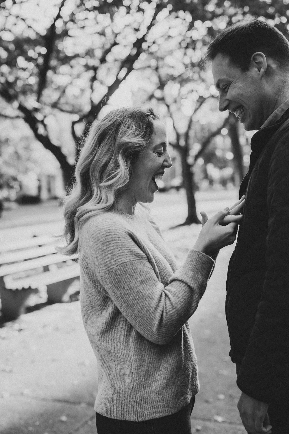 Black and white photo of a laughing couple sharing a joyful moment together in a park during autumn.