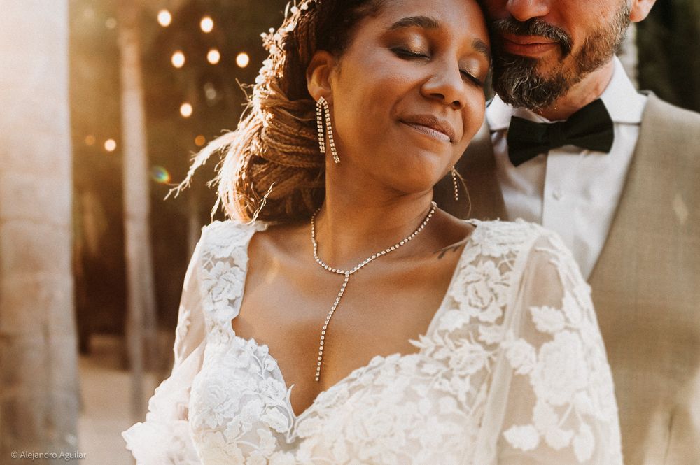 Bride in lace wedding dress and diamond necklace with groom in tuxedo at outdoor wedding ceremony.