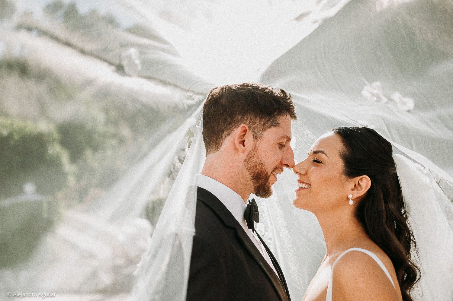 Bride and groom share a romantic moment under a flowing veil outdoors on their wedding day.