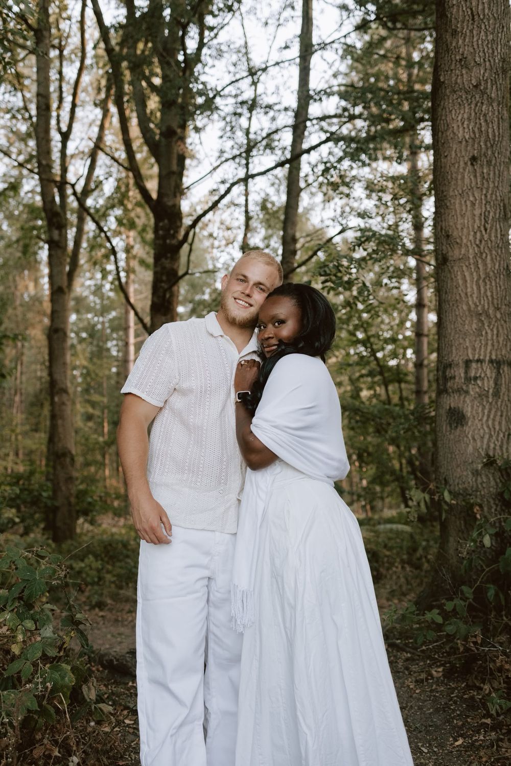 Couple standing together among the trees during a woodland engagement shoot