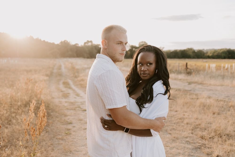 Couple embracing in a sunlit field during a relaxed engagement shoot