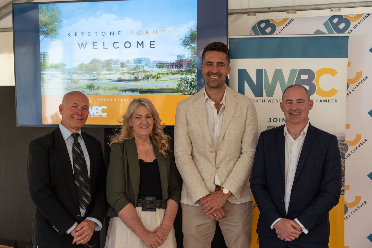 Four professionals posing for photo at NWBC Keystone Forum welcome event with promotional banner backdrop.