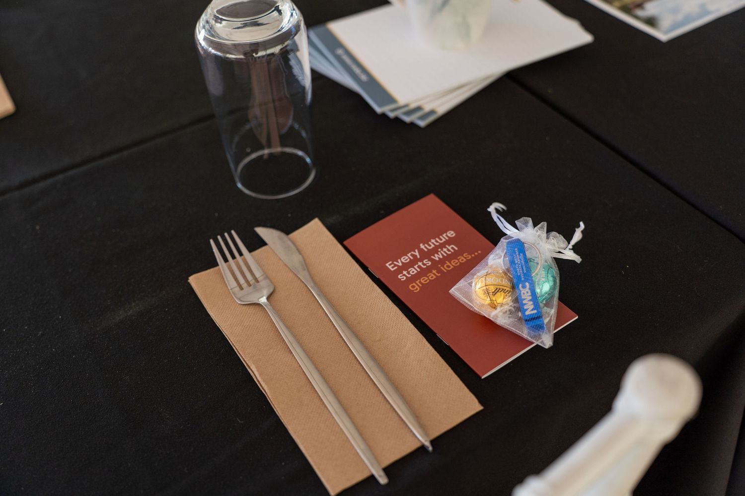 Black table setting with cutlery, glass, and small motivational card at corporate dining event.