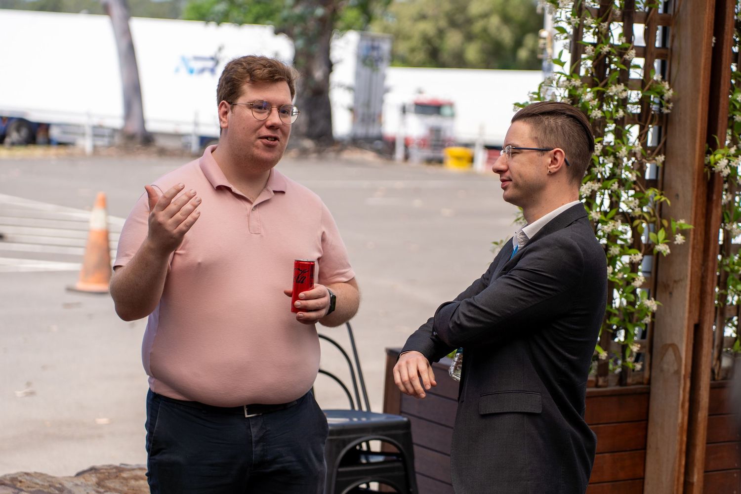 Two men in casual and formal attire having conversation outside wooden building at business networking event.