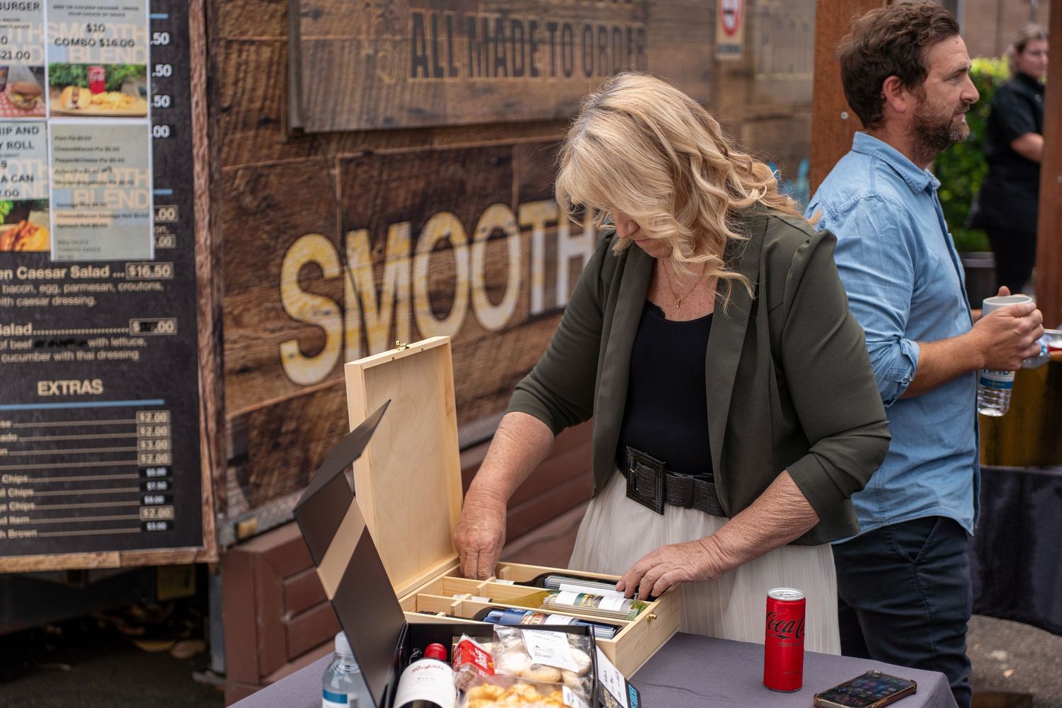 Woman examining food in a box at an outdoor smoothie bar market stall.