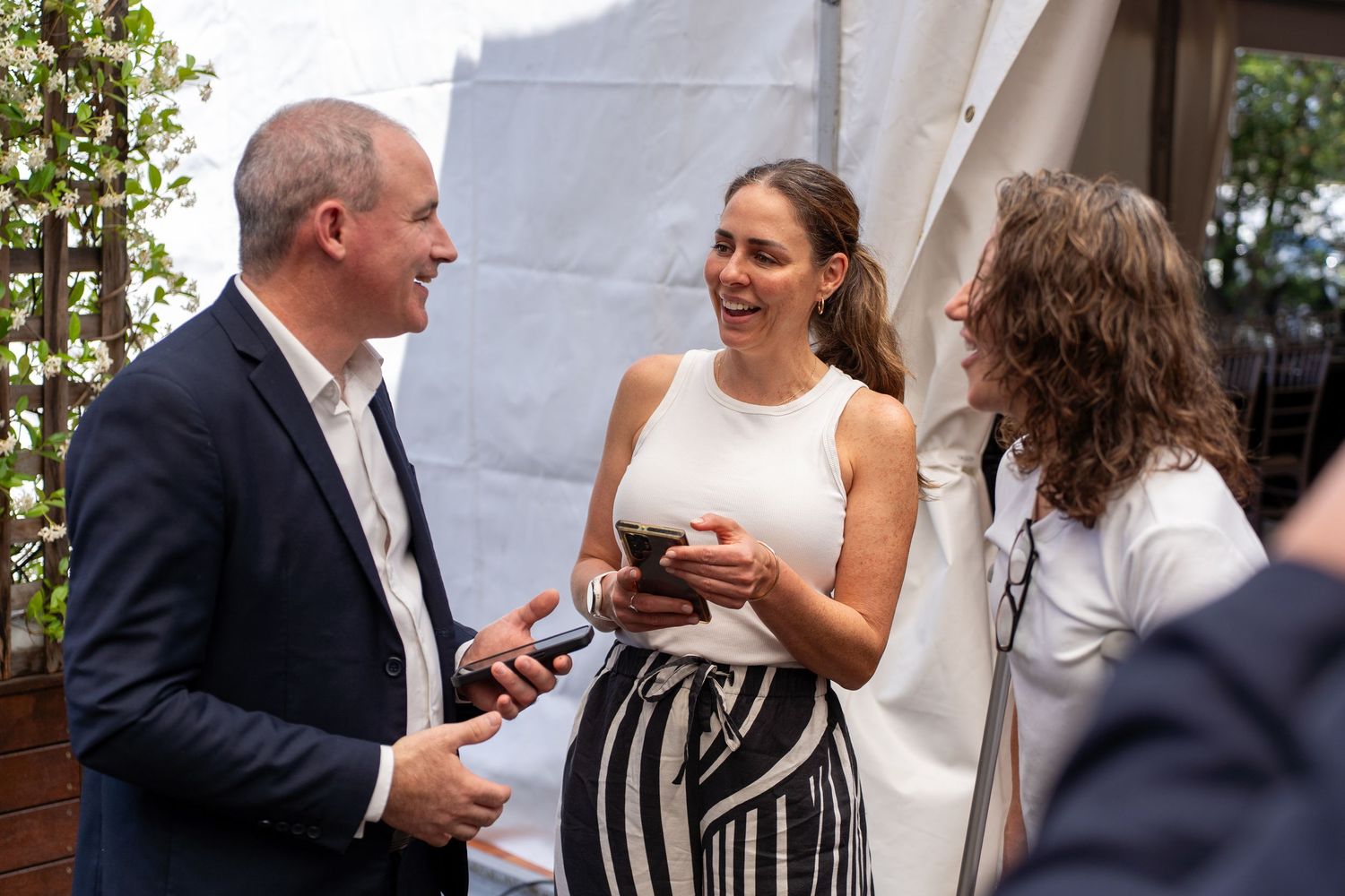Three professionals smiling and networking at an outdoor business event.