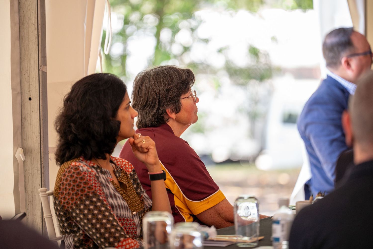 Two women seated together listening attentively at an indoor business luncheon event.