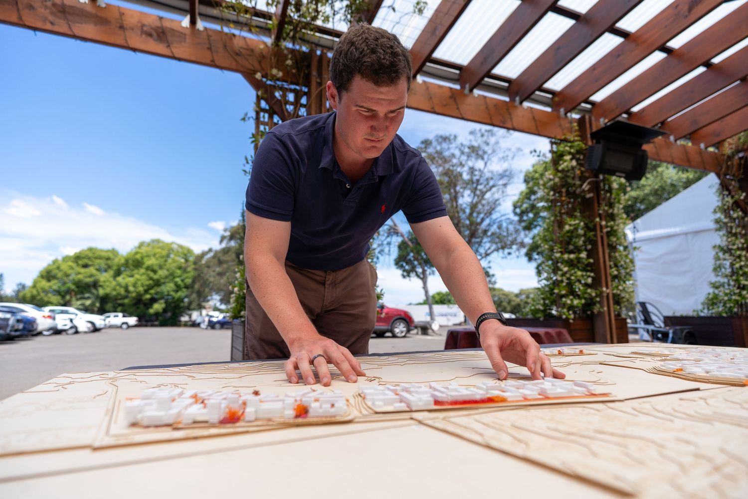 Man leaning over large urban planning map laid out on outdoor table under pergola.