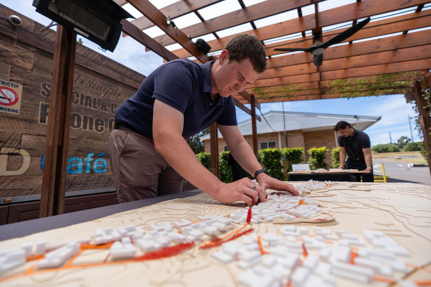 Man marking details on large city map spread across outdoor table at planning event.