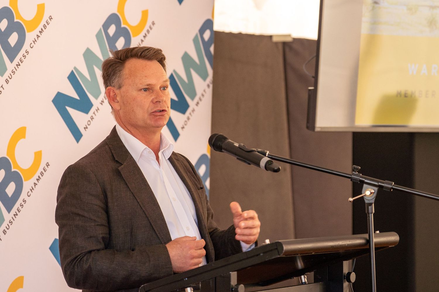 Professional speaker presenting at NWBC business chamber event at indoor podium.