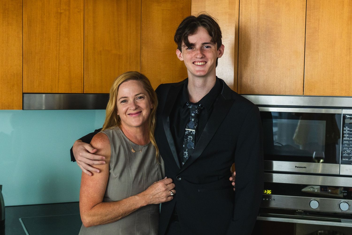 Mother and teenage son posing together smiling in a kitchen before a formal event.