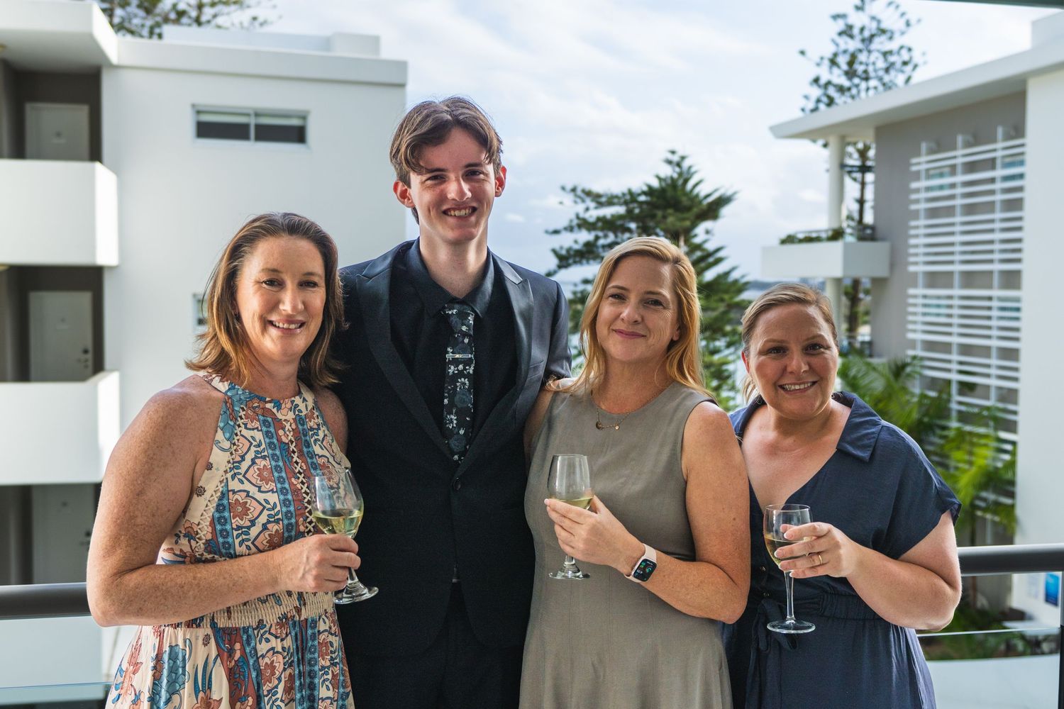 Group of four adults smiling and holding champagne glasses on an outdoor balcony.