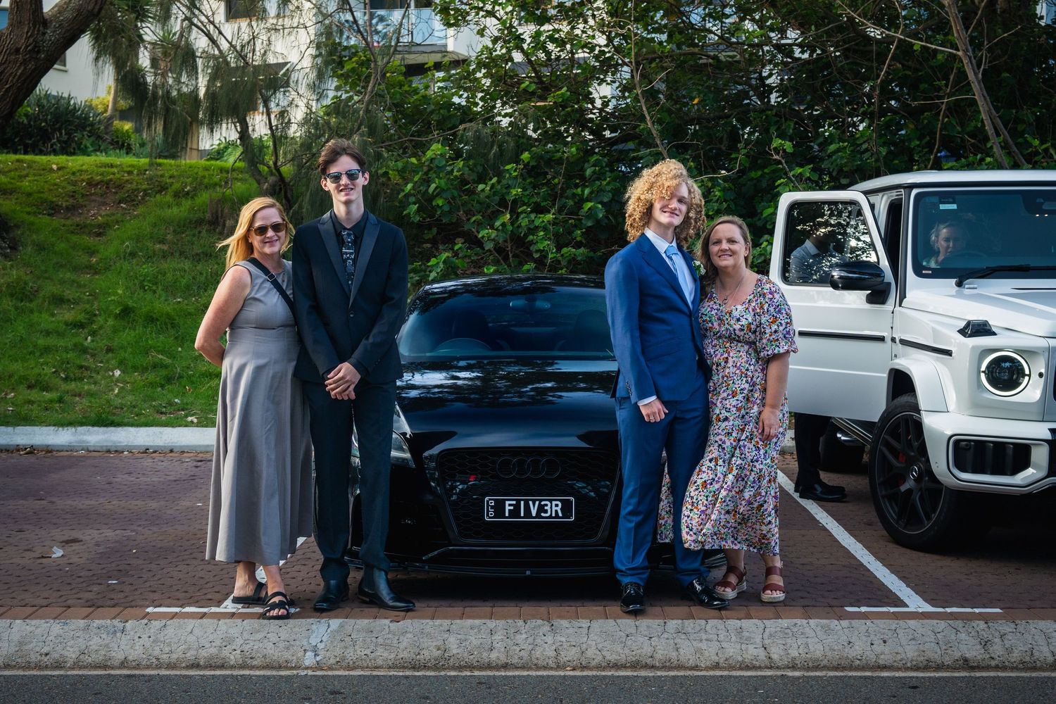 Family group of four poses beside a black Audi FIV3R before a school formal event.