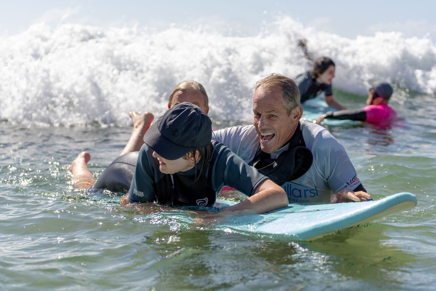 An instructor helps a child ride a surfboard through ocean waves during an adaptive surfing lesson.