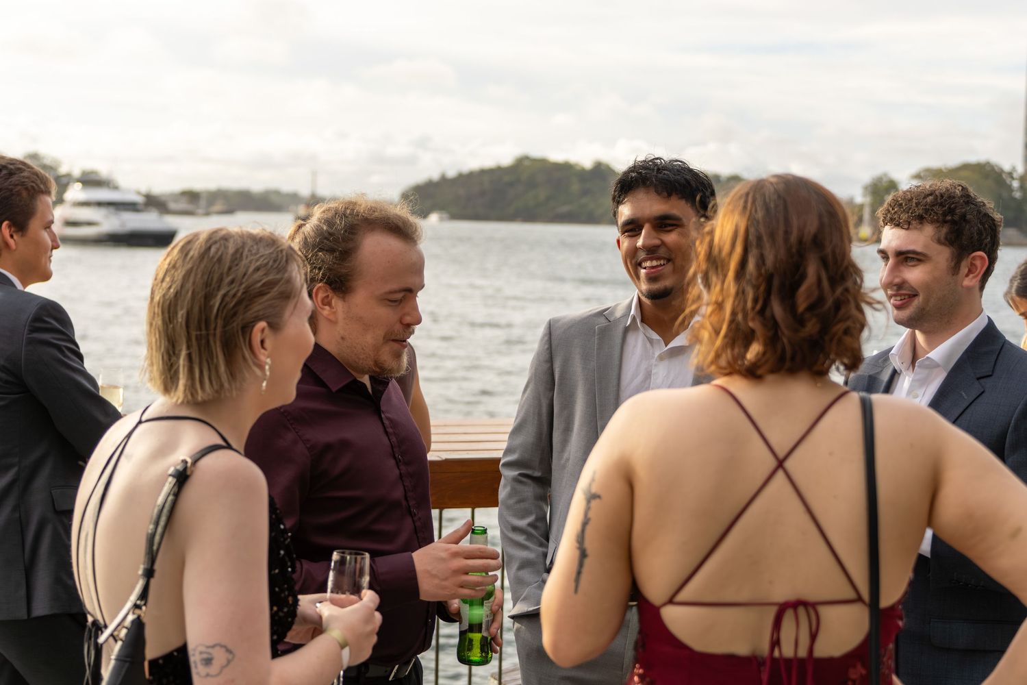 Elegantly dressed guests socialise on a waterfront venue during a formal evening event.