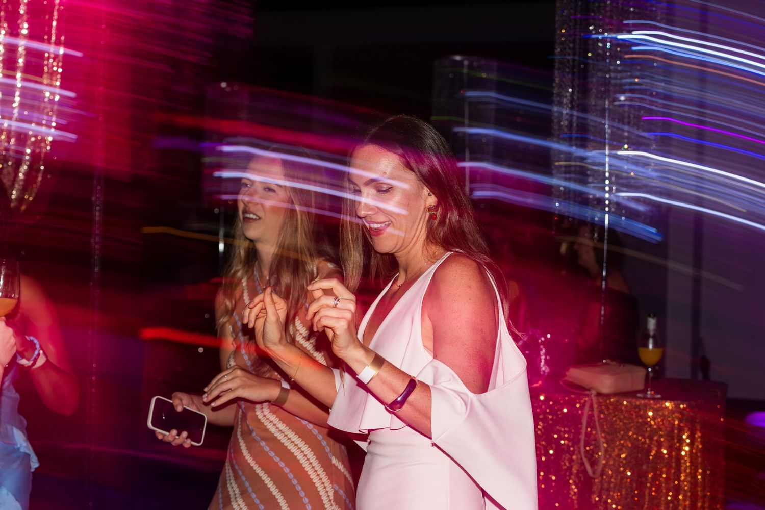 Two women dancing under colorful lights at a vibrant evening event.