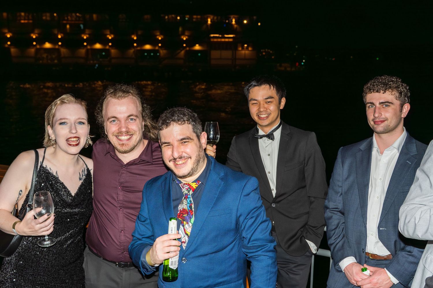 Group of five friends posing outdoors at night with drinks at a party.