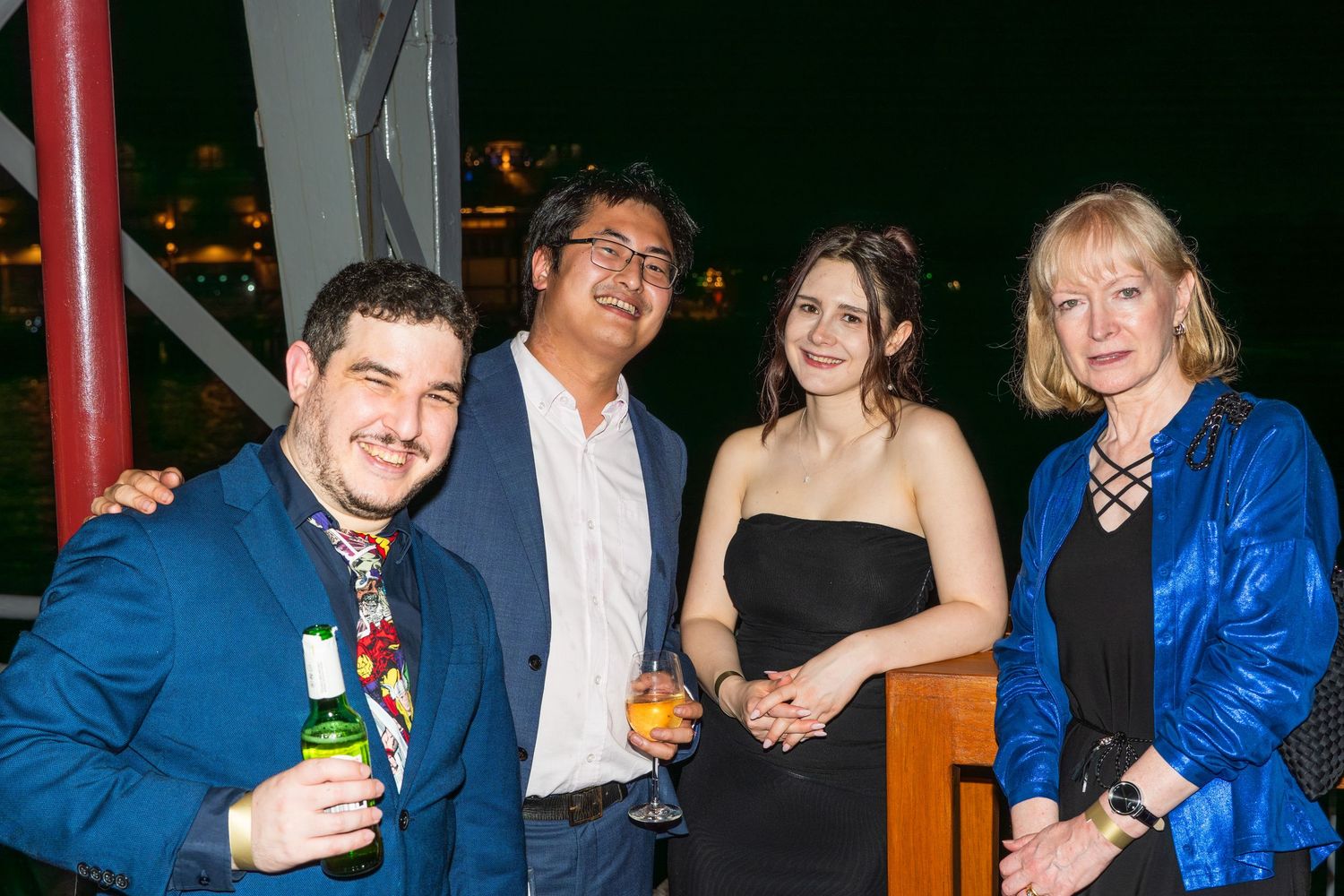 Four guests smile and pose with drinks at an elegant outdoor evening event.