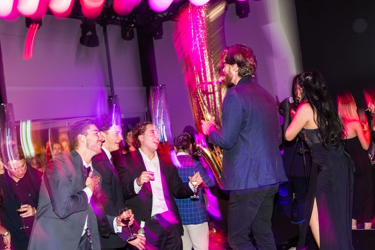 Guests mingle and laugh together under colorful pink lights at a formal gala event.