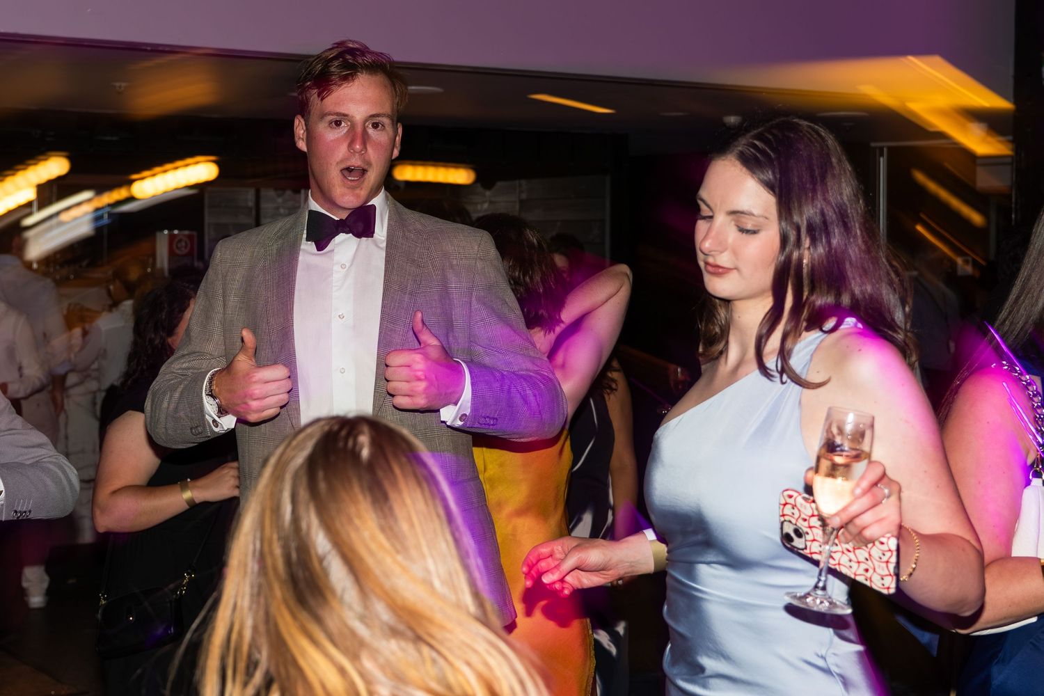 A man in a tuxedo and woman in blue dress dance and socialize at a formal party.