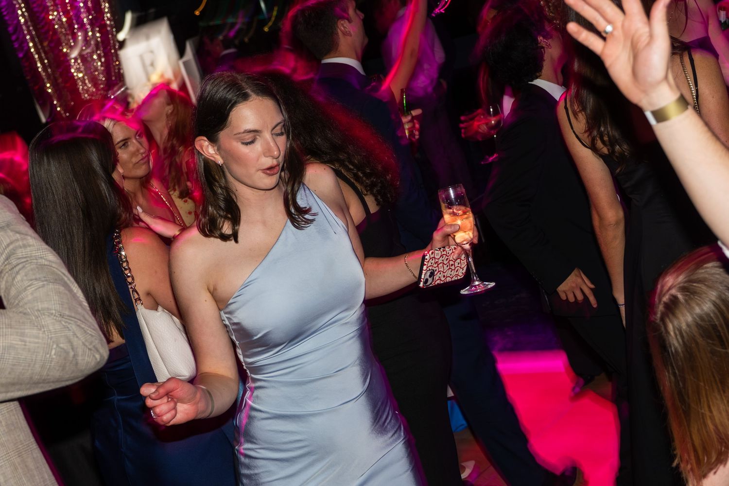 A woman in a silver dress dances elegantly while holding a champagne glass at a gala.