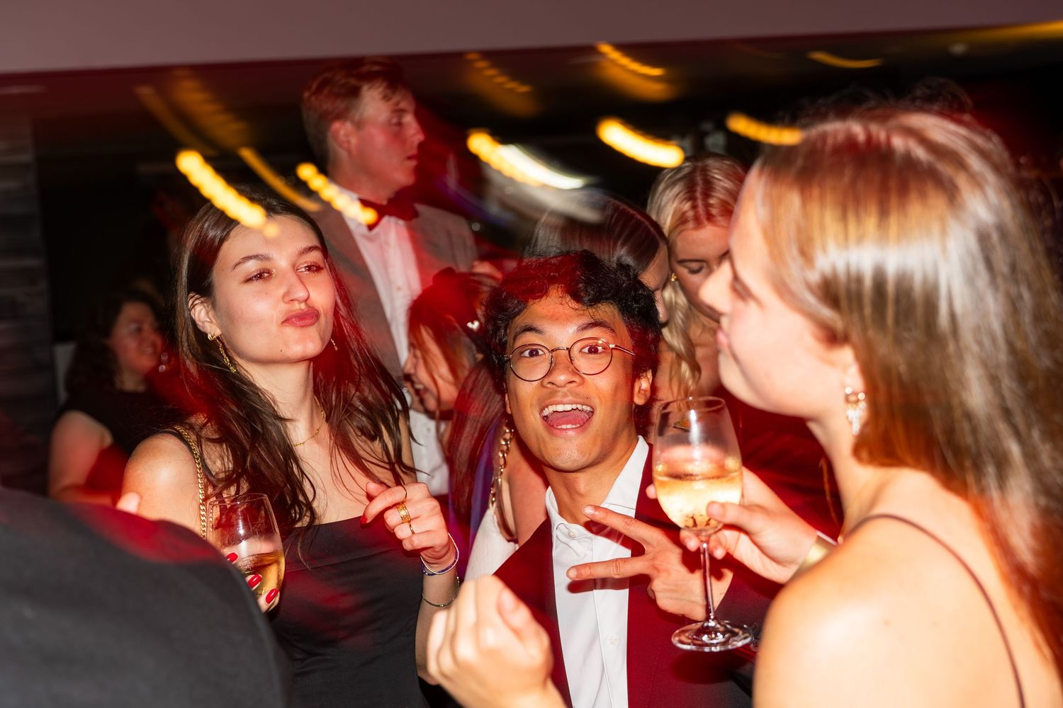 Three young guests laugh and celebrate together with champagne at a formal evening event.