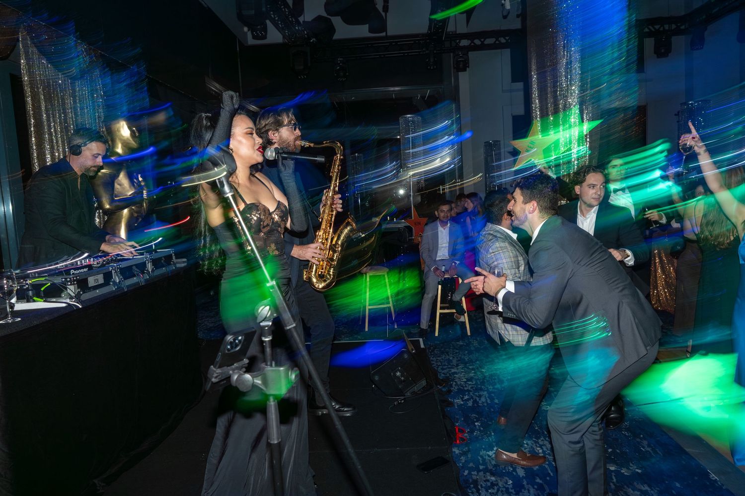 A saxophonist performs under green laser lights as guests dance at an energetic party.