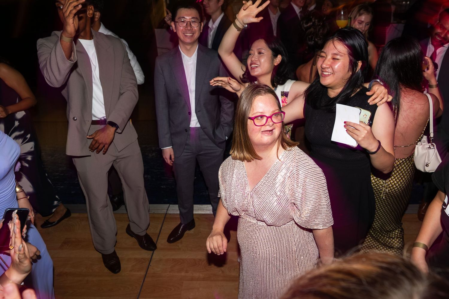 Guests in formal wear dance joyfully together under warm lights at an evening celebration.
