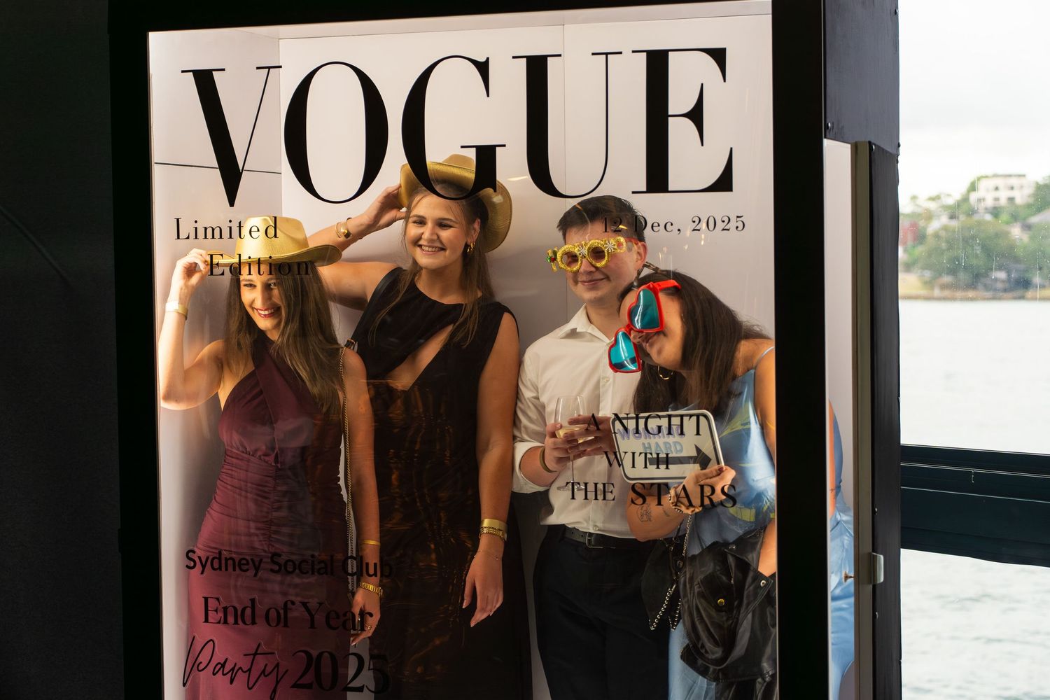 Four guests posing playfully in front of a Vogue Limited Edition photo booth backdrop.