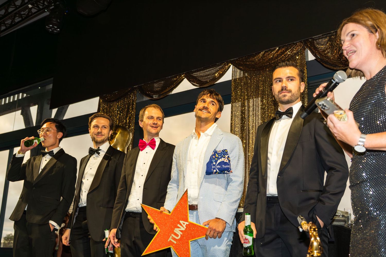 Group of formally dressed people on stage at an awards ceremony with a glowing star prop.