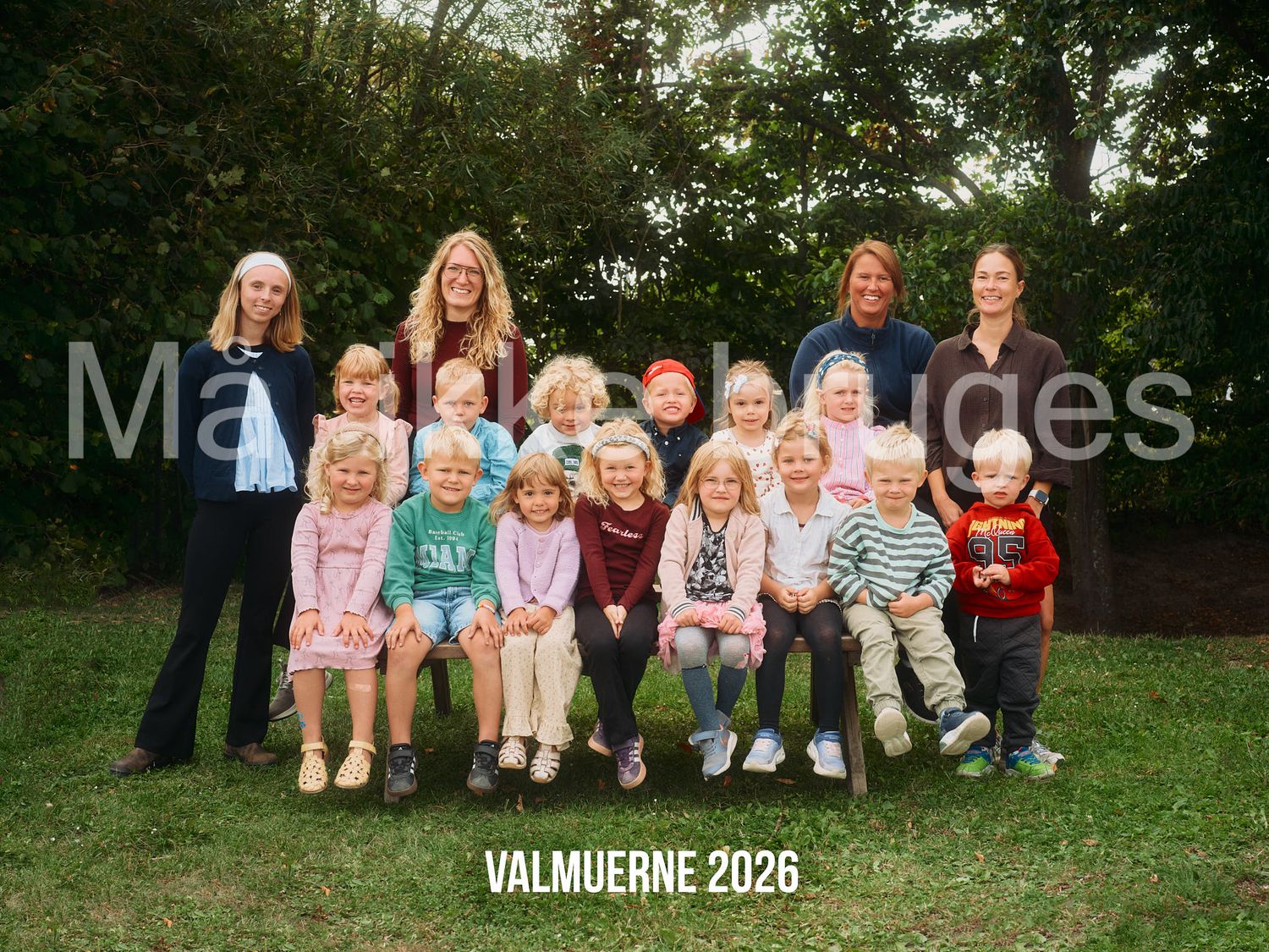 Group photo of children and teachers outdoors labeled Valmuerne 2026, posing together on a bench in a garden setting.