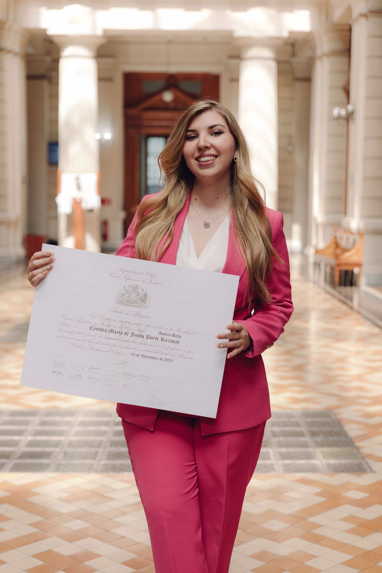 Smiling woman in pink blazer proudly displaying her graduation diploma certificate.
