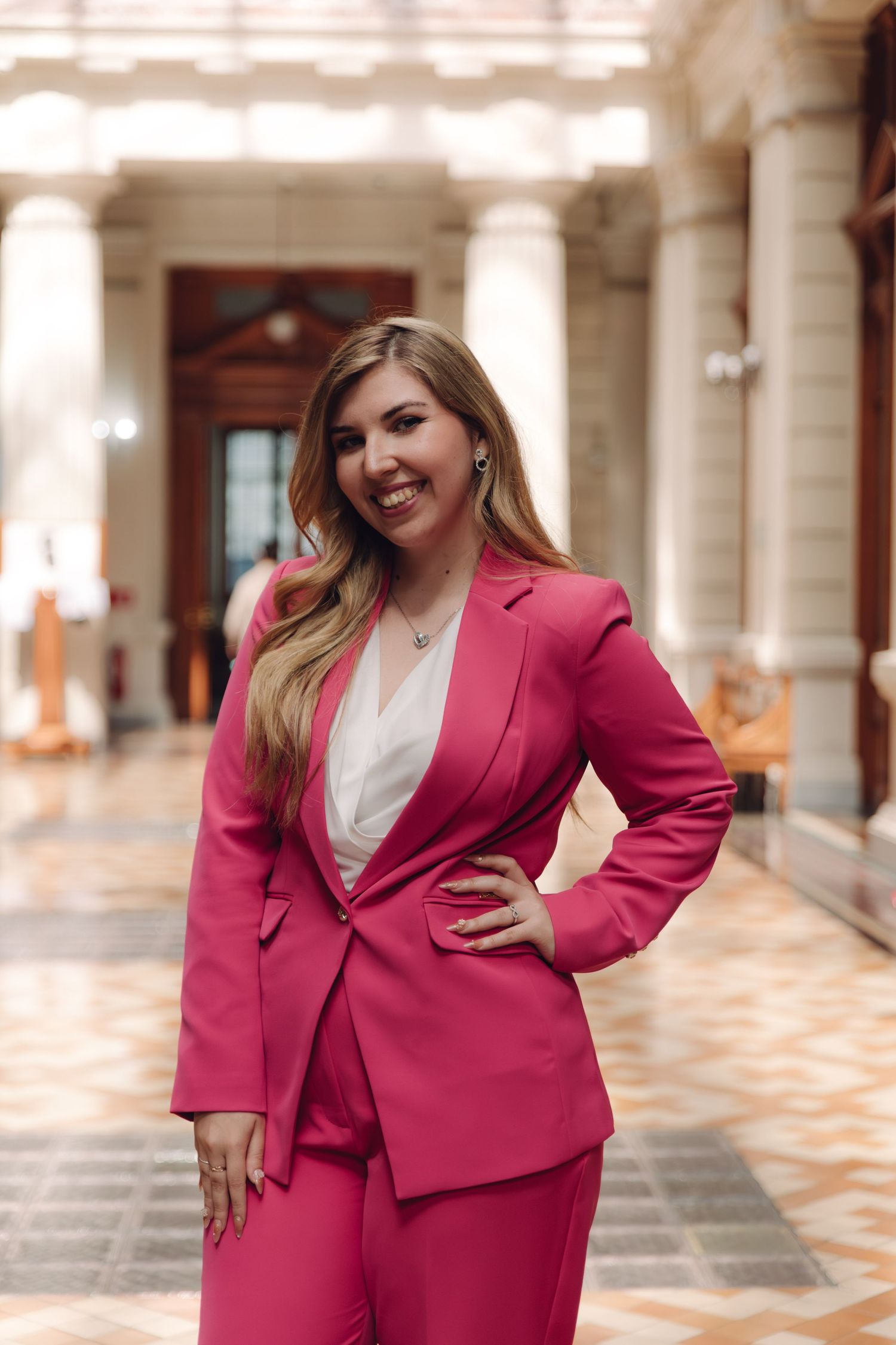 Confident smiling woman in bright pink business suit posing in elegant hallway.