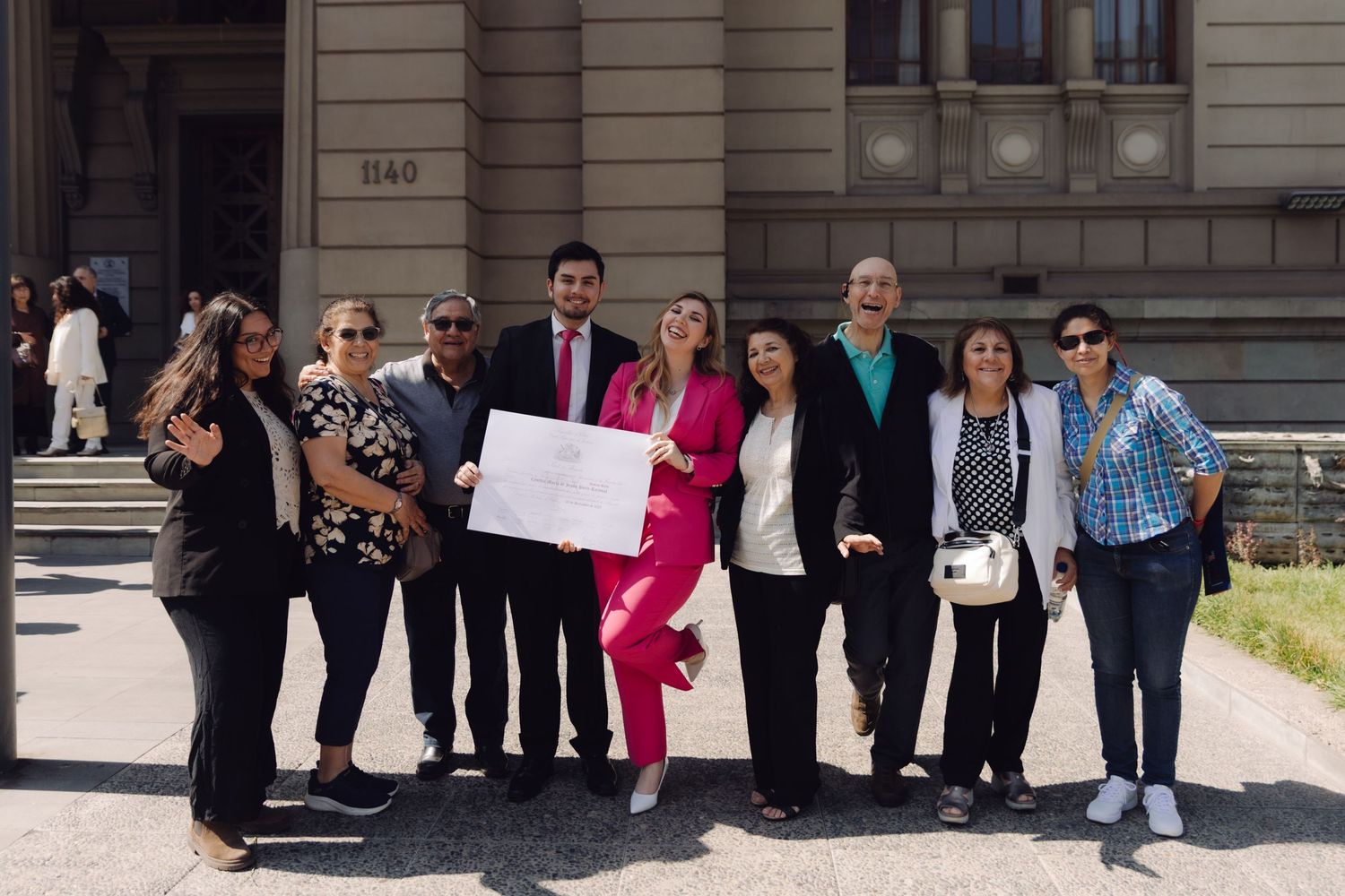Group of people posing together outside a stone building holding a document.