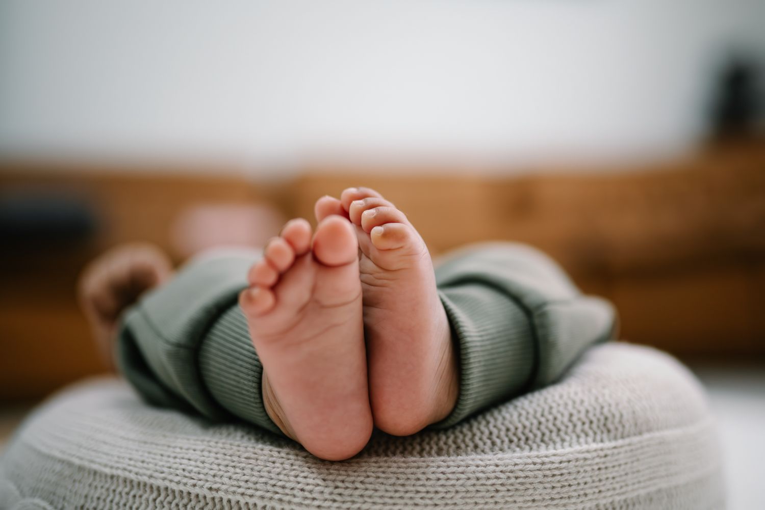 Close-up of tiny newborn baby feet in a green knit onesie, resting on a soft blanket.