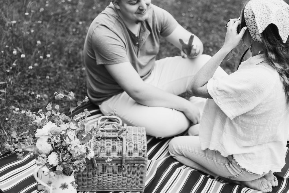 Two women enjoying a picnic on a blanket with a wicker basket and flowers in a black and white photo.