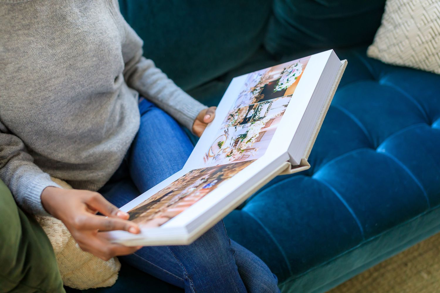 Person holding open photo album while sitting on blue tufted couch.