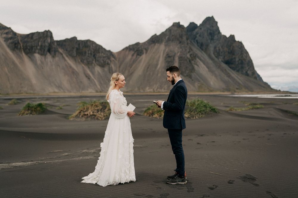 Bride and groom exchanging vows on black sand beach with dramatic Vestrahorn mountain backdrop in Iceland.