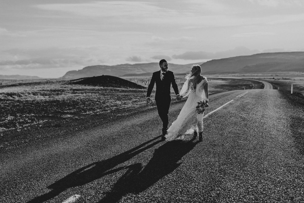Black and white photo of bride and groom walking hand in hand down an empty road in Iceland.