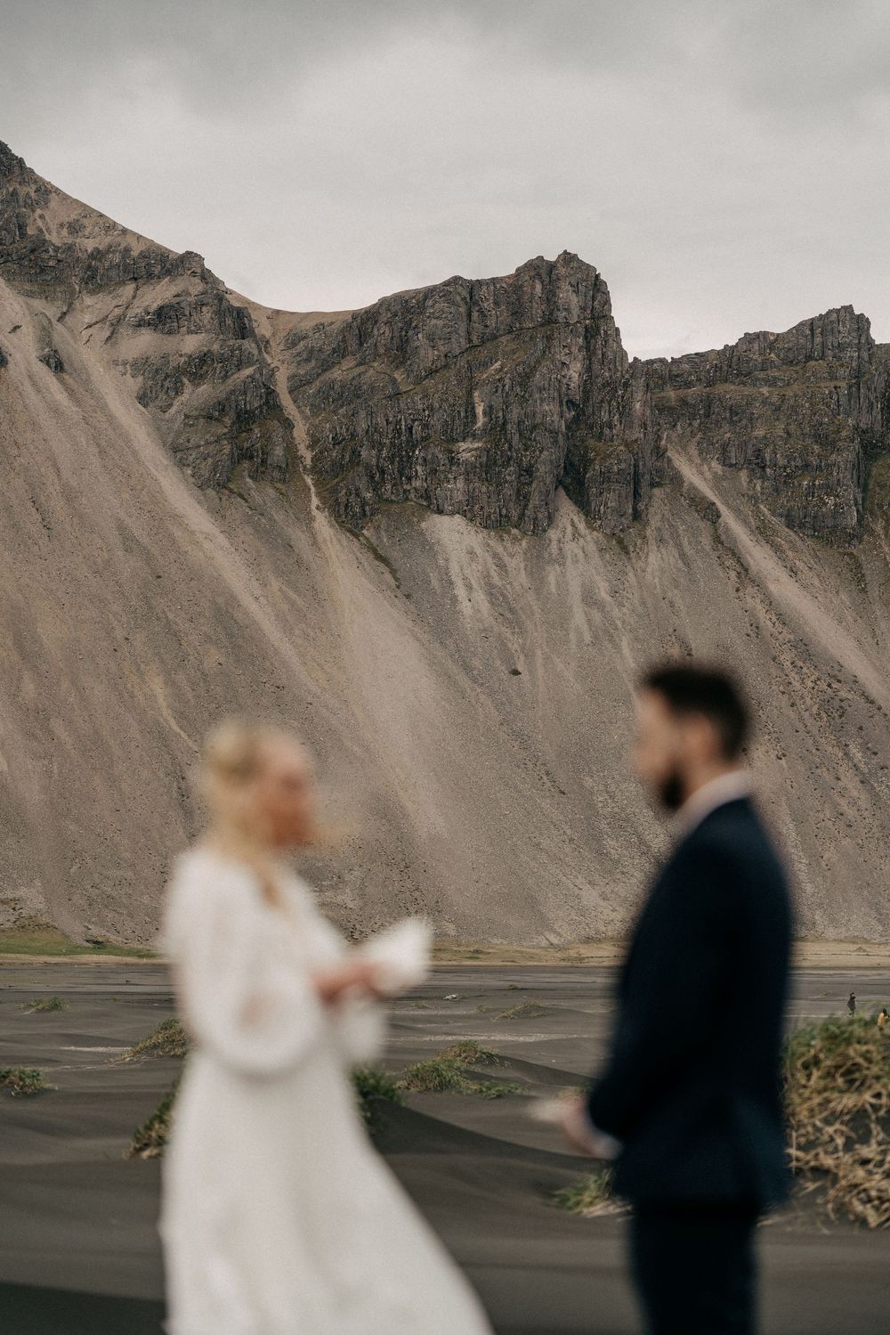 Bride and groom standing before the dramatic rocky slopes of Vestrahorn mountain on black sand beach Iceland.