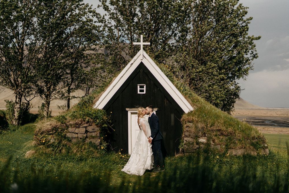 Bride and groom kissing outside a charming traditional turf church surrounded by greenery in Iceland.