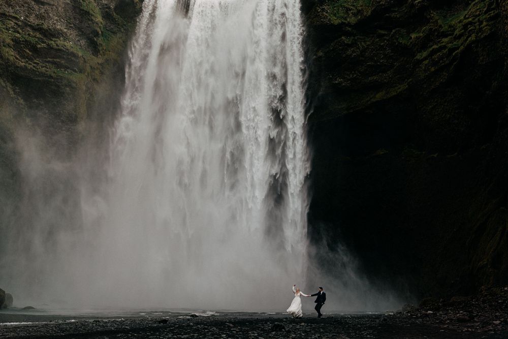 Wedding couple dancing in the mist beneath the towering Skogafoss waterfall in Iceland.