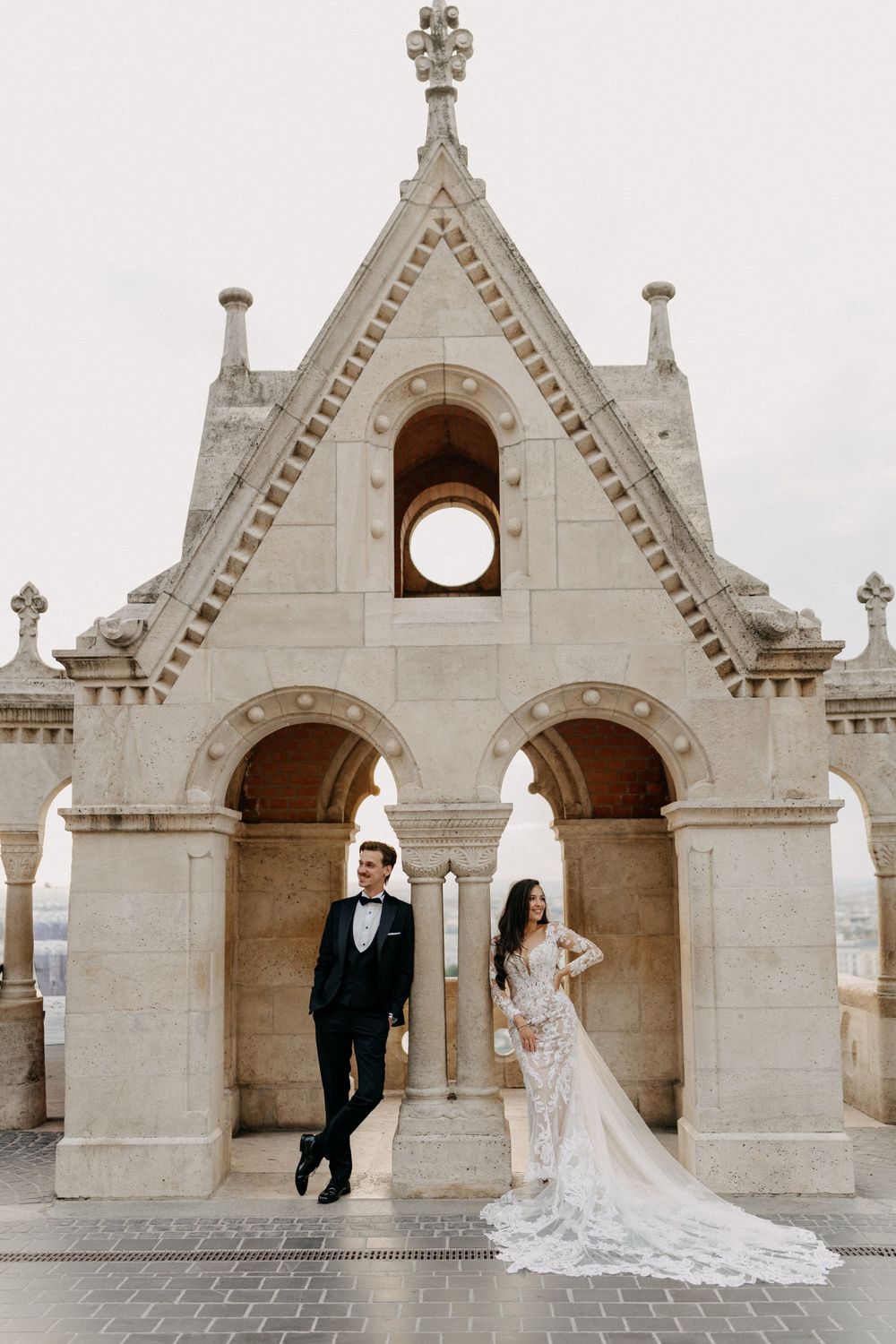 Bride and groom posing under Gothic stone arches at Fishermans Bastion Budapest on their wedding day.