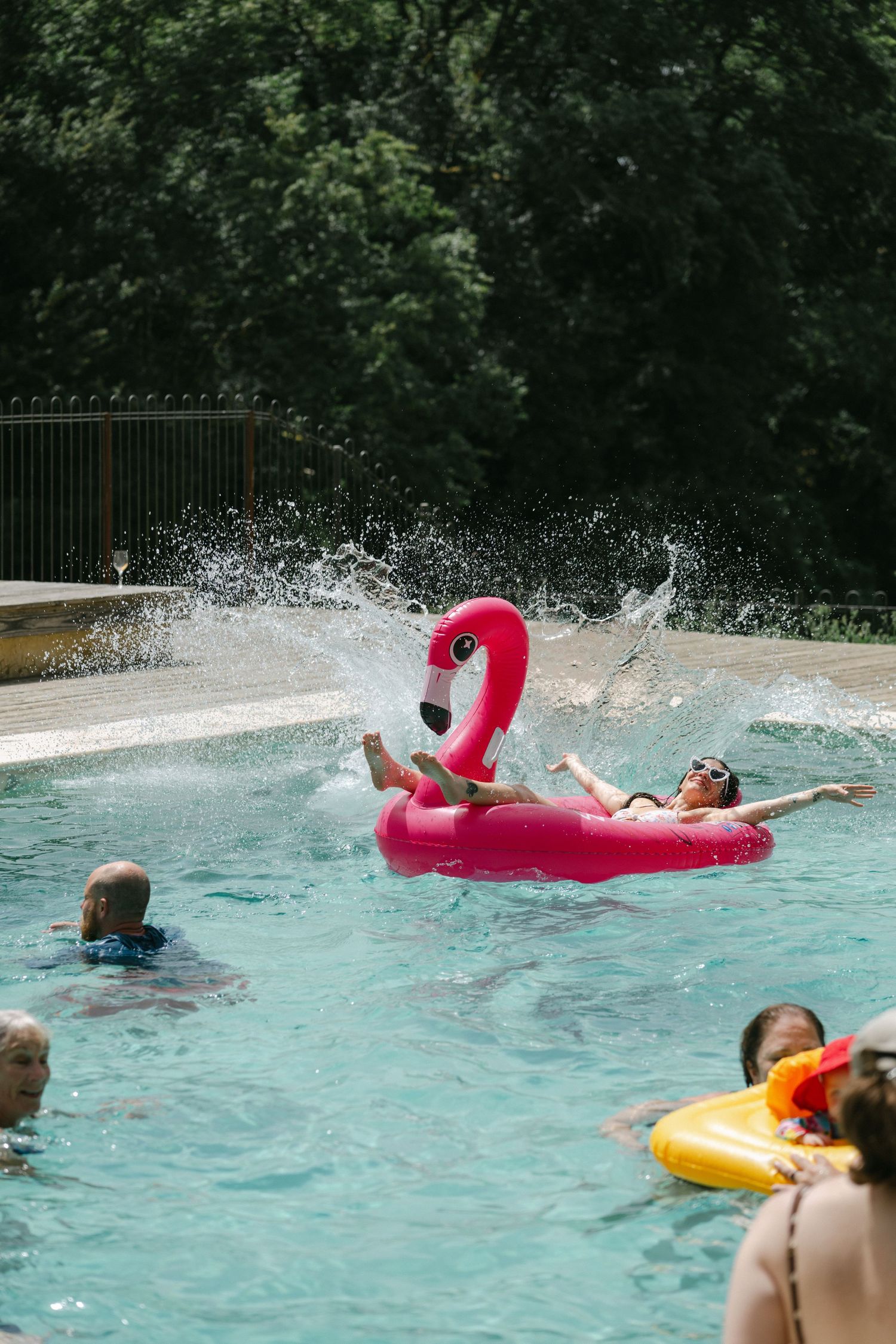 People enjoying a summer pool party with a pink flamingo inflatable float creating a big water splash.