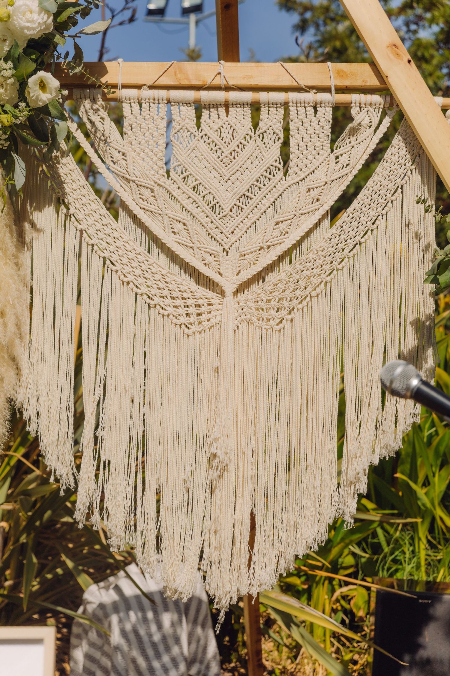 Close-up of an intricate cream macrame wall hanging displayed on a wooden triangular wedding ceremony arch.