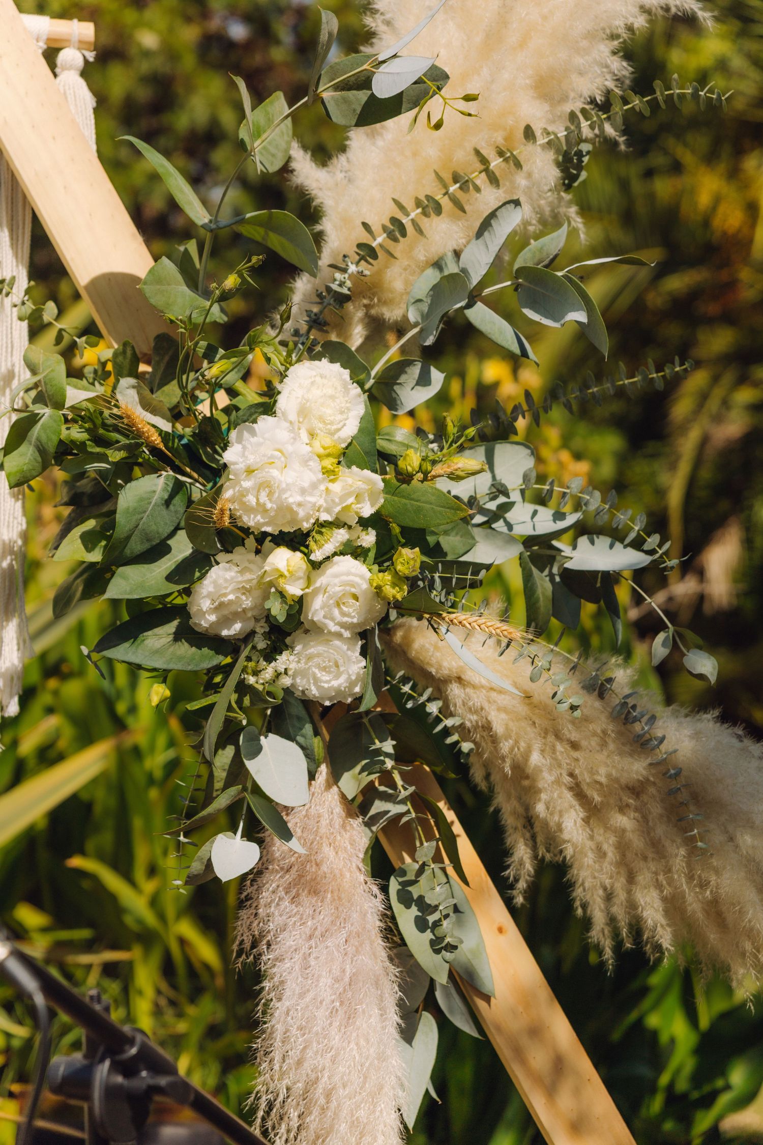 Elegant white roses and eucalyptus floral arrangement with pampas grass decorating a wooden wedding arch.