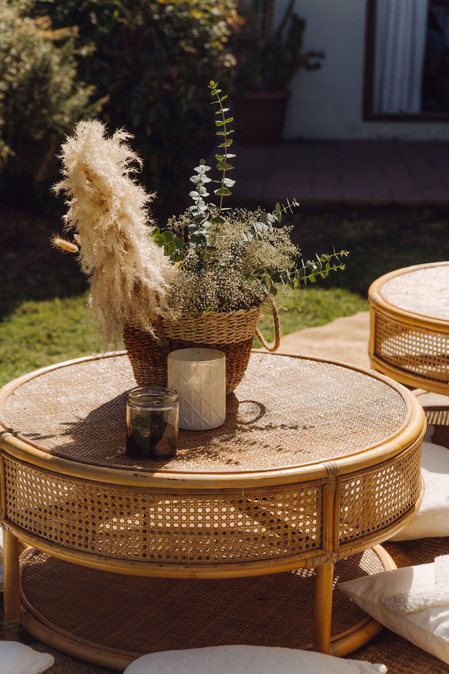 Boho-style rattan coffee table with wicker basket of pampas grass, eucalyptus, and candles in sunny garden.